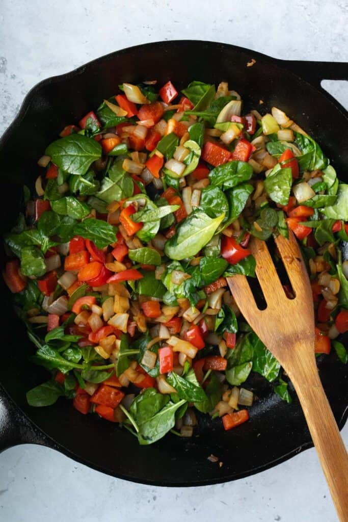 sautéed onion, red bell pepper and spinach in a cast iron skillet