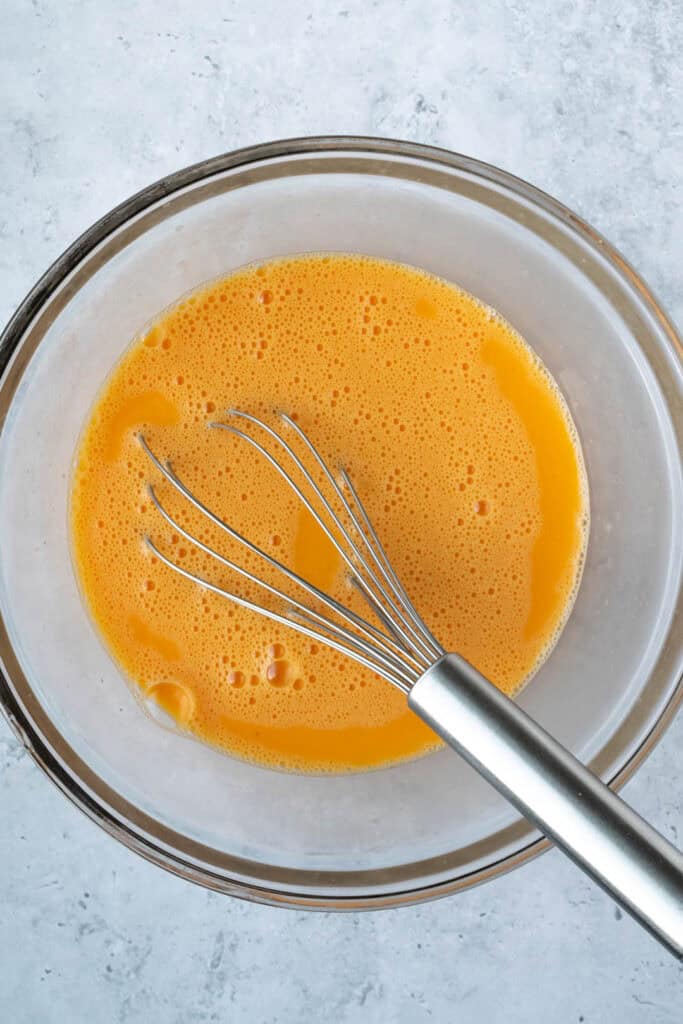 whisked eggs in a glass bowl with a metal whisk