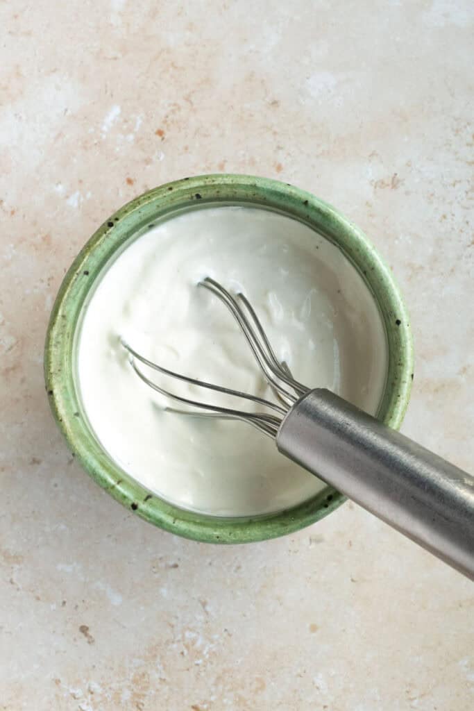 garlic yogurt sauce in a green bowl with a whisk.