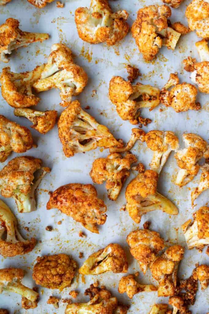 raw cauliflower florets tossed in spices on a sheet pan.