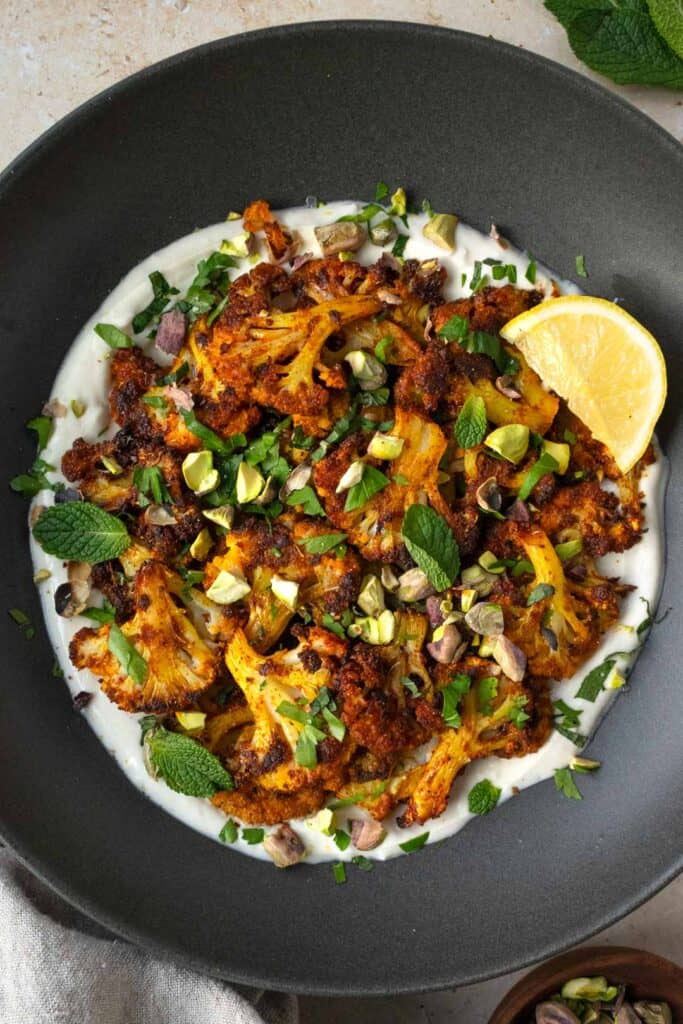 garlic yogurt topped with cauliflower and herbs on a black dish.