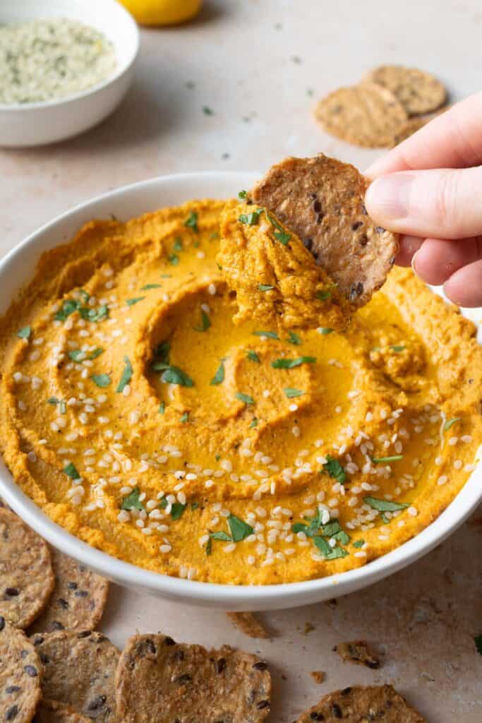 a hand holding a cracker with roasted carrot dip